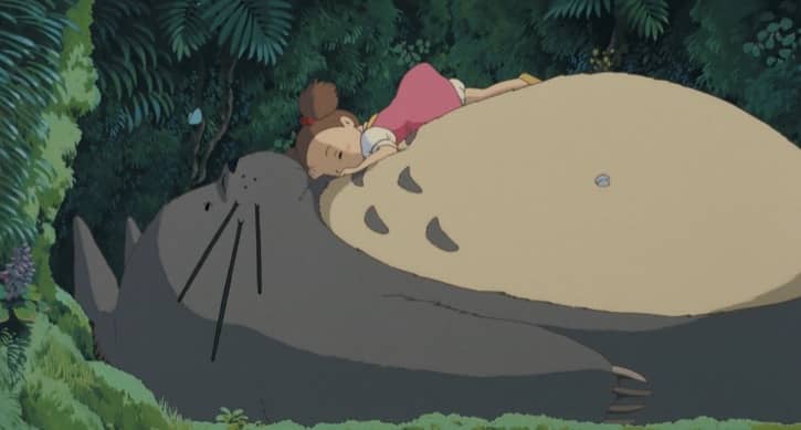Totoro resting on his back laying on the ground and Mei Kusakabe laying on top of him like a big pillow